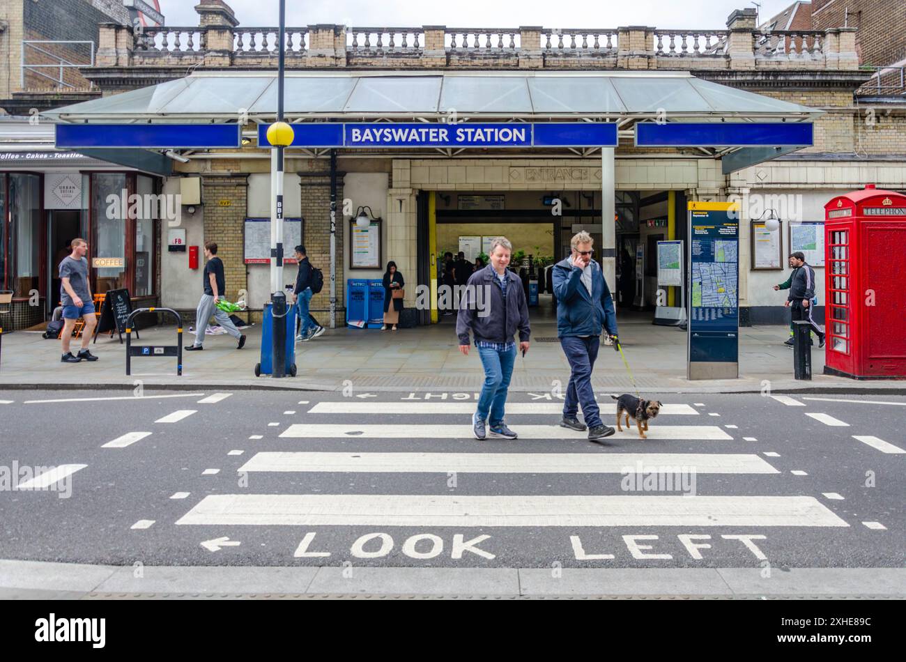 Männer, die einen Hund laufen, überqueren die Straße über einen Fußgängerübergang vor der Bayswater London U-Bahnstation am Queensway Stockfoto