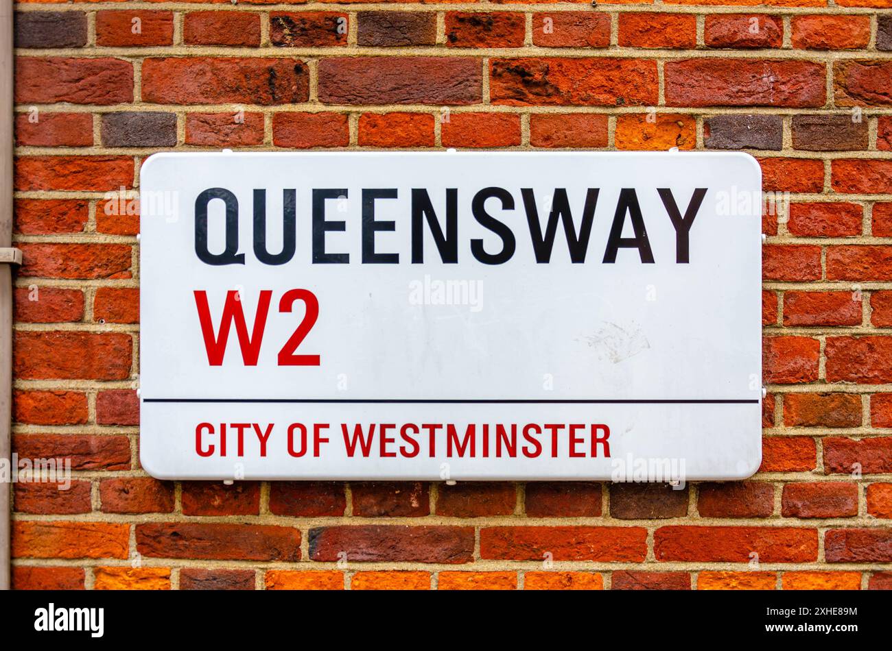 Das Straßenschild von Queensway ist an einer roten Backsteinmauer in der City of Westminster, London, Großbritannien, angebracht Stockfoto