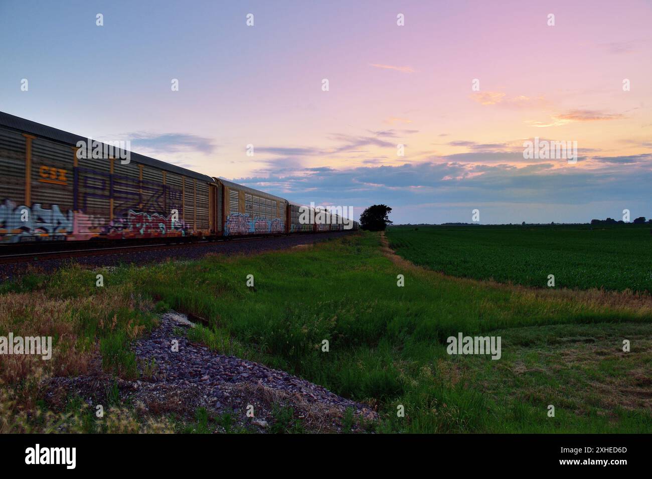 Cortland, Illinois, USA. Ein Auto-Rack-Güterzug in westlicher Richtung verwischt glitschig, während er in der Abenddämmerung durch den ländlichen Nordosten von Illinois fährt. Stockfoto