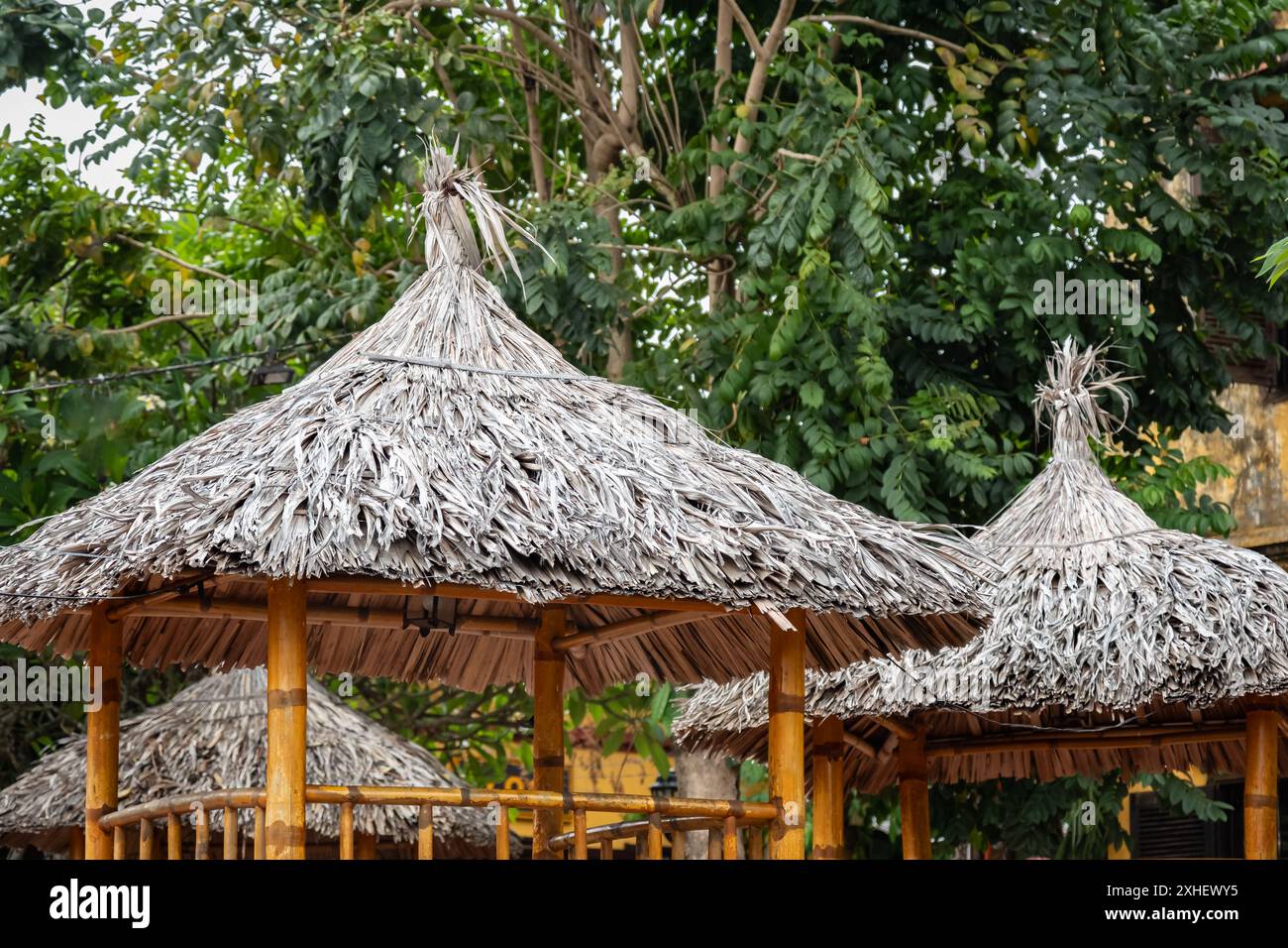 Das Dach besteht aus Schilf auf einem hölzernen Pavillon. Ein hölzernes Ferienhaus. Ein sonniger Sommertag. Strandpavillon aus Bambus und getrockneten Blättern. Grasblatt Stockfoto