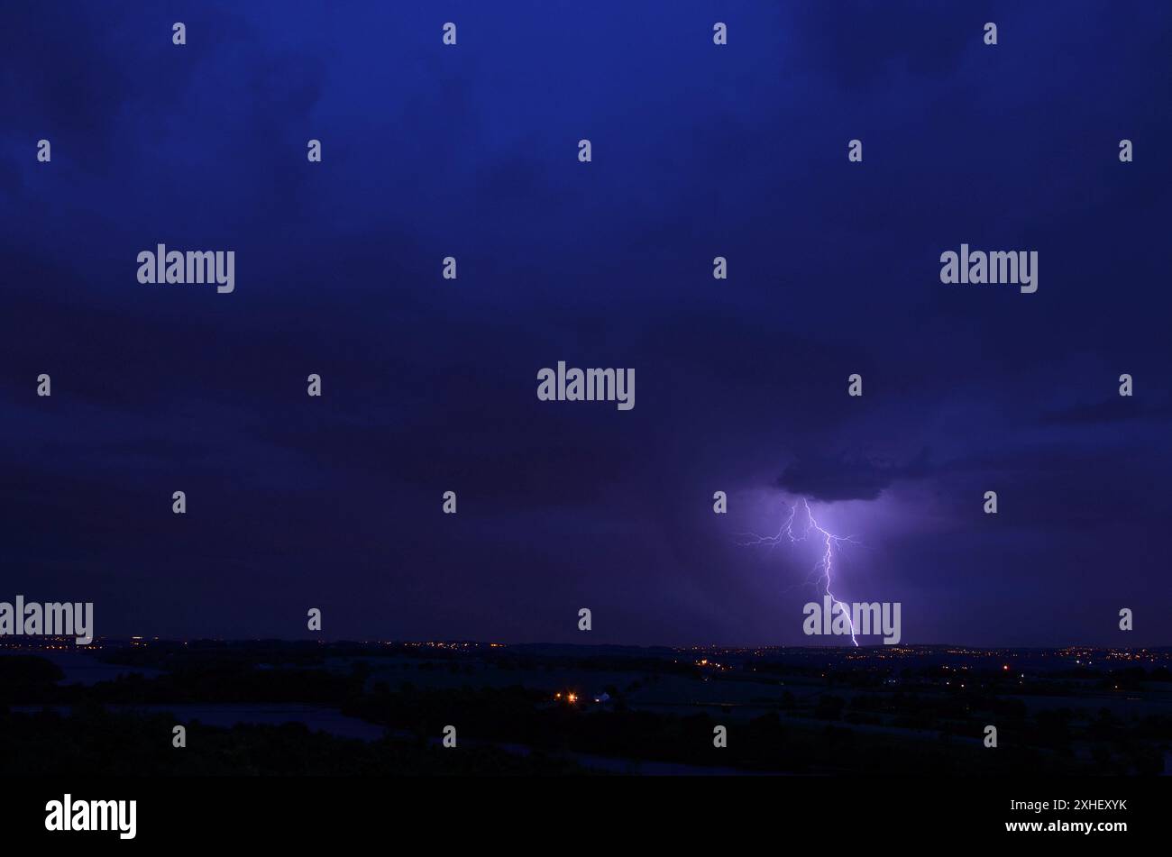 Ein Gabelbolzen trifft in der Entfernung auf den Boden. Die Lichter der Stadt sind sichtbar. Es ist Abend oder Dämmerung und wird dunkel. Das Saphirblau des Himmels. Stockfoto