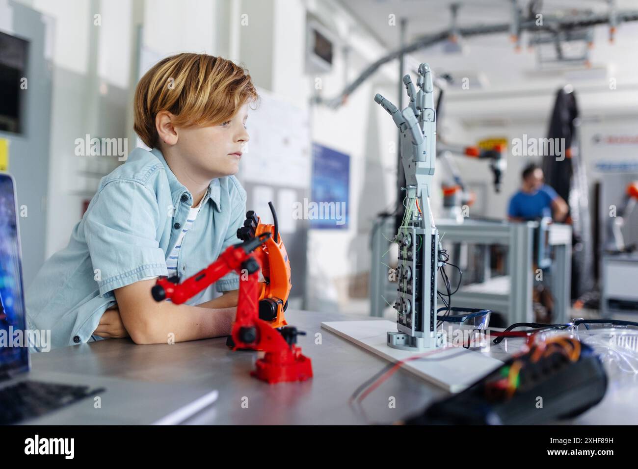 Porträt eines Schuljungen, der Roboterarm und Hand aussieht, Roboterclub nach der Schule. Kinder, die Robotik in der Grundschule lernen. Wissenschaft für Kinder. Stockfoto