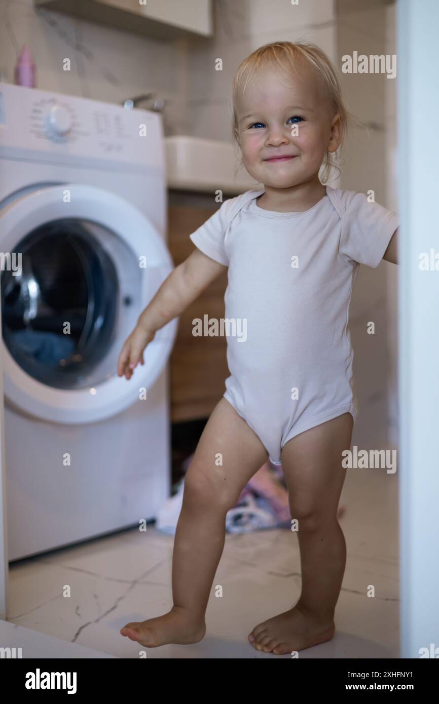 Zwei Jahre altes Kind, das Hausaufgaben macht. Waschmaschine wird geladen. Stockfoto