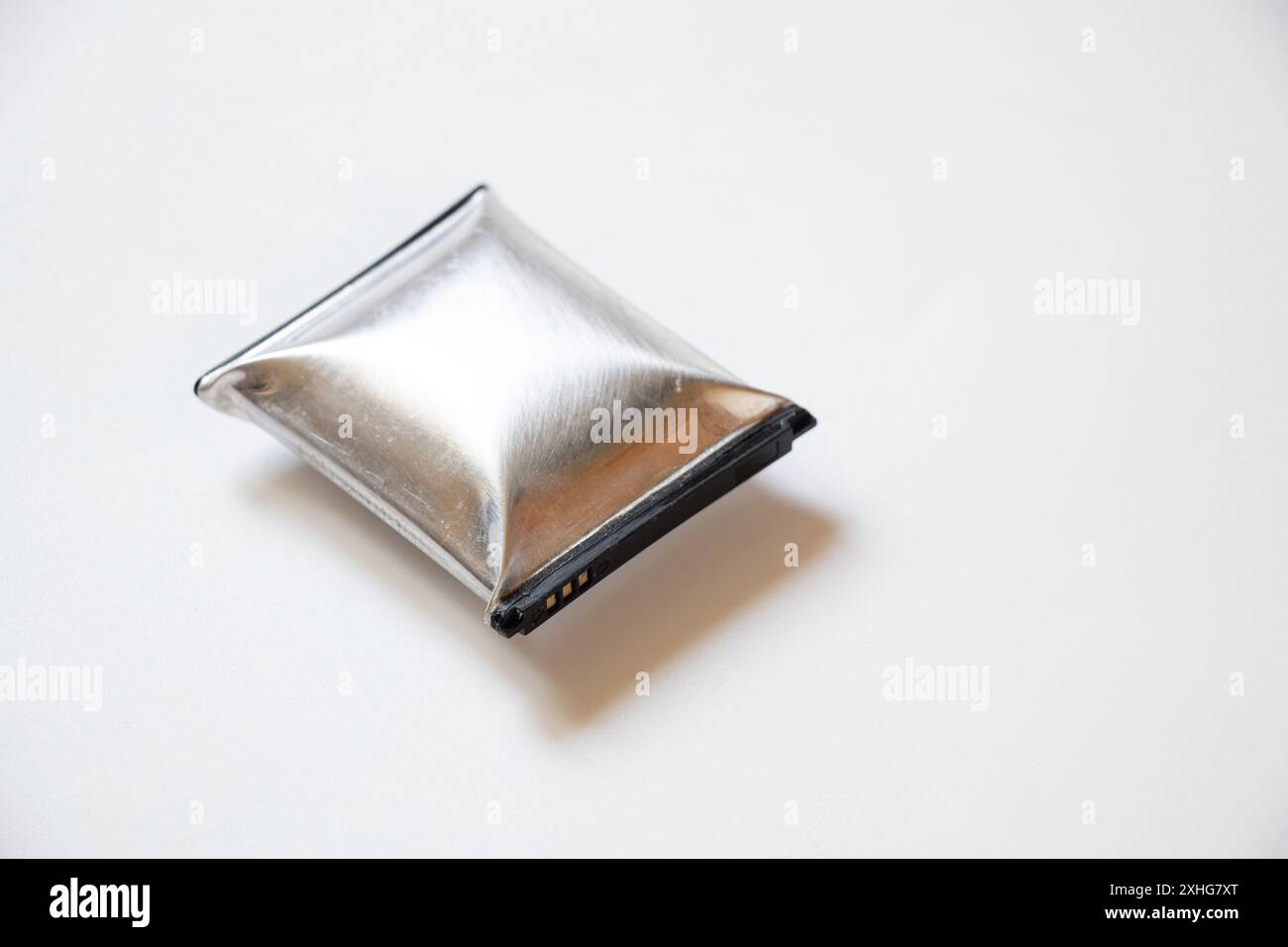 Eine durch Überhitzung geschwollene Telefonbatterie liegt auf einem weißen Hintergrund, die Telefonbatterie ist aufgeblasen Stockfoto