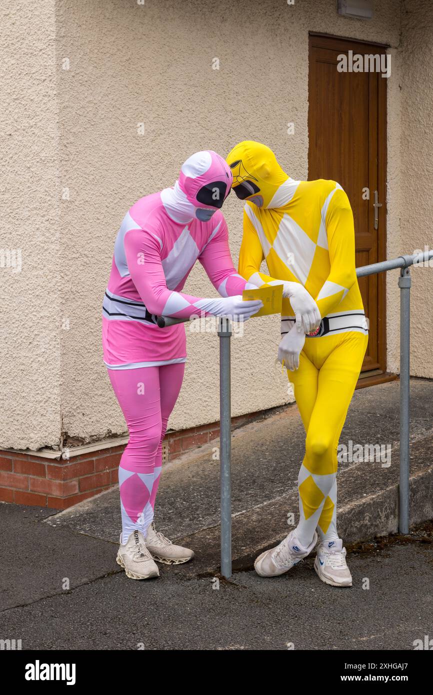 Zwei Männer in rosafarbenen und gelben Power Rangers hautnahe Ganzkörperanzüge, die bei einem lokalen Karneval in Wales, Großbritannien, gesehen wurden Stockfoto