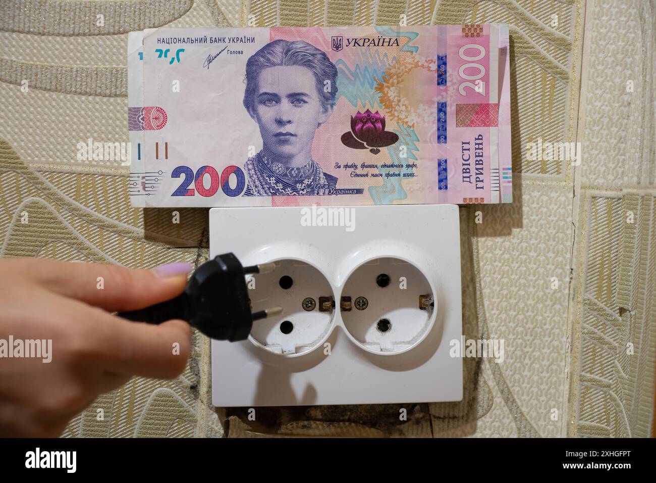 Die Hand einer Frau hält einen Stecker in der Nähe einer Steckdose neben Hrywnja in einer Wohnung in der Ukraine, die Zölle steigen Stockfoto Die Hand einer Frau hält einen Stecker in der Nähe einer Steckdose neben Hrywnja in einer Wohnung in der Ukraine, die Zölle steigen Stockfoto
