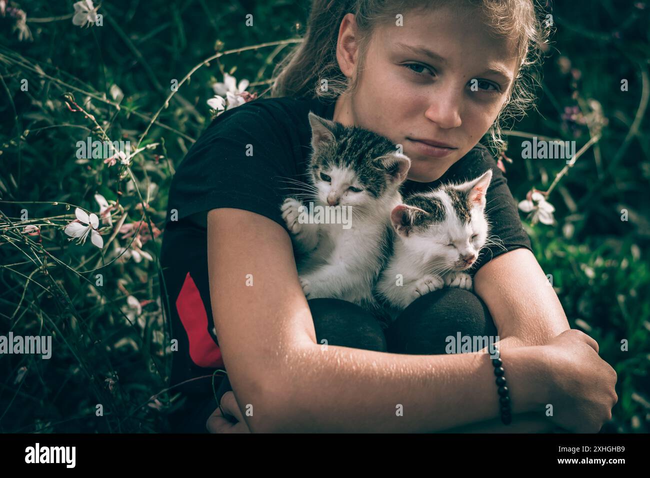 Blondes Mädchen, das kleine, entzückende Katzen im Garten hält Stockfoto