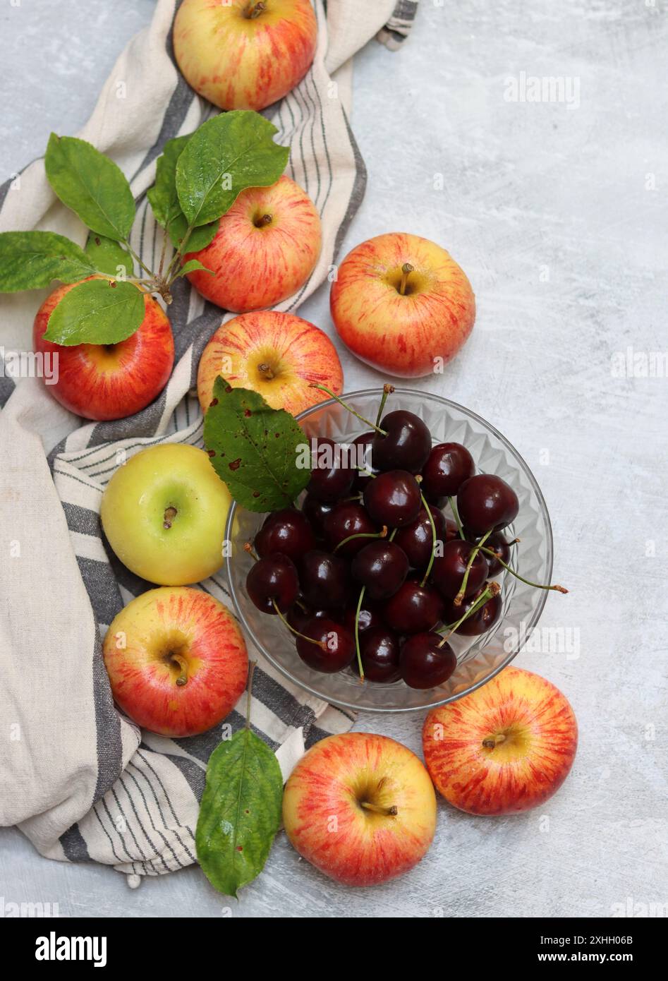 Rote Äpfel und Kirschen auf einem Teller auf hellem Hintergrund mit Kopierraum. Nahaufnahme der Sommerfrüchte. Fresh-Konzept. Reife rote Äpfel Stockfoto