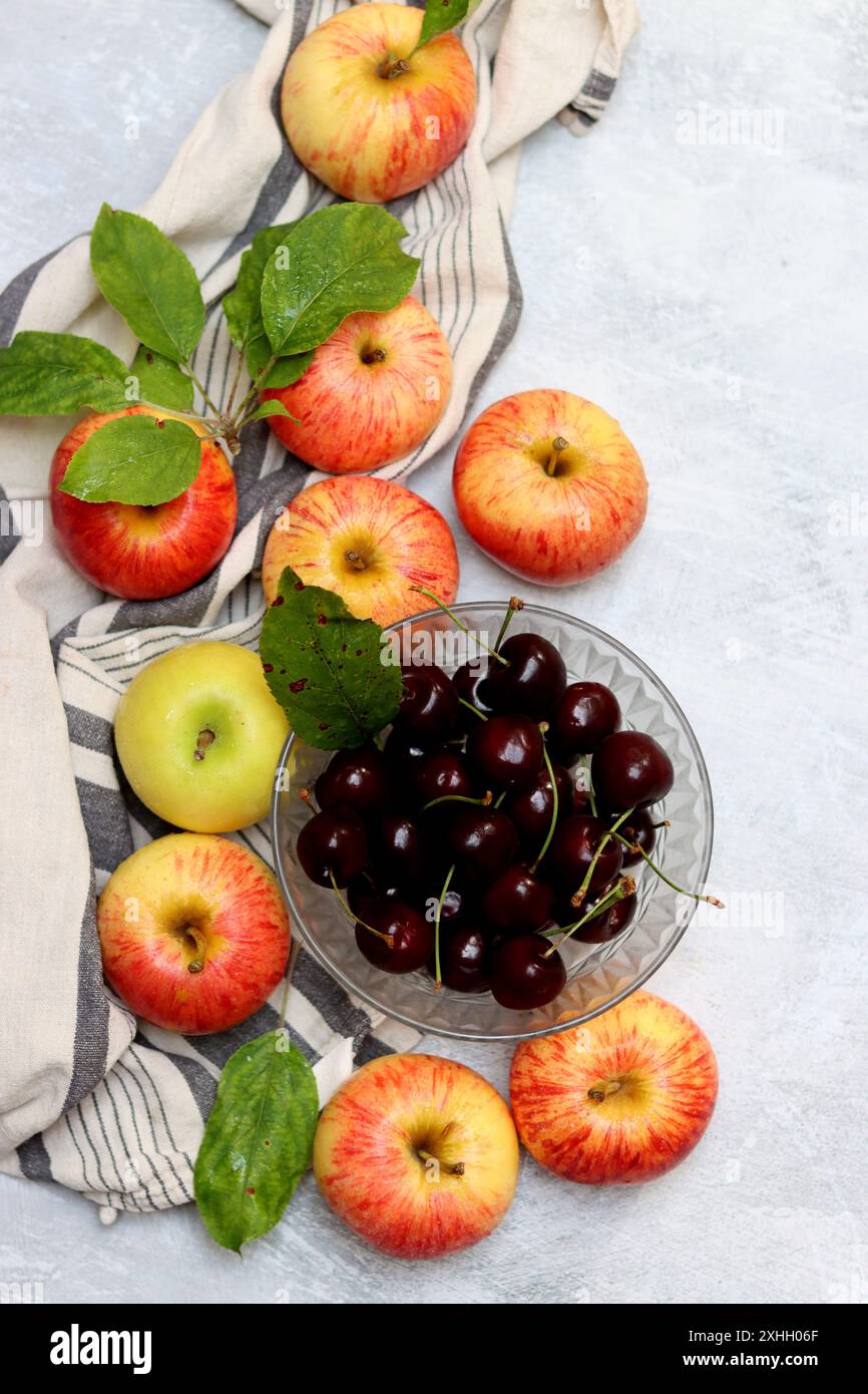 Rote Äpfel und Kirschen auf einem Teller auf hellem Hintergrund mit Kopierraum. Nahaufnahme der Sommerfrüchte. Fresh-Konzept. Reife rote Äpfel Stockfoto