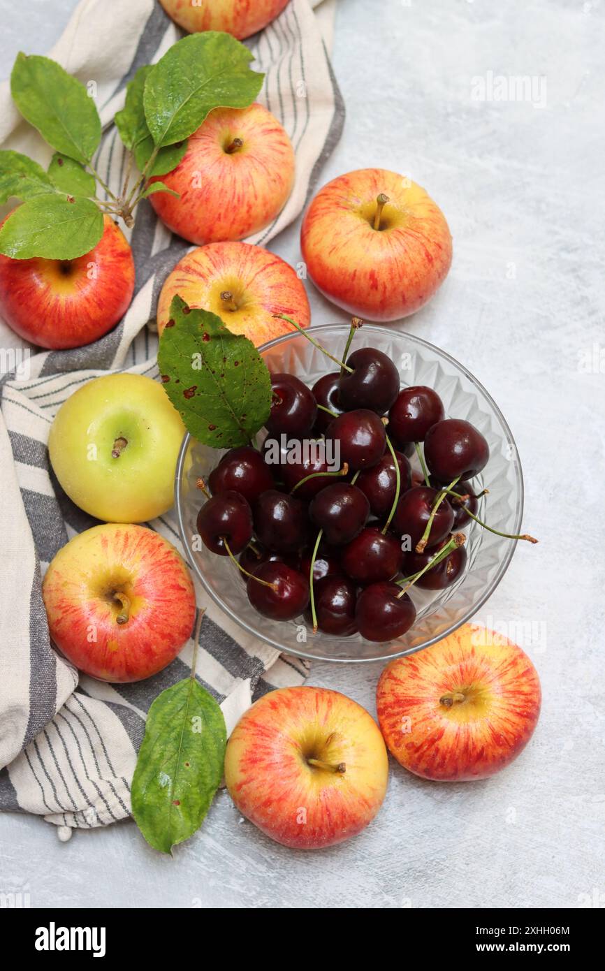 Rote Äpfel und Kirschen auf einem Teller auf hellem Hintergrund mit Kopierraum. Nahaufnahme der Sommerfrüchte. Fresh-Konzept. Reife rote Äpfel Stockfoto