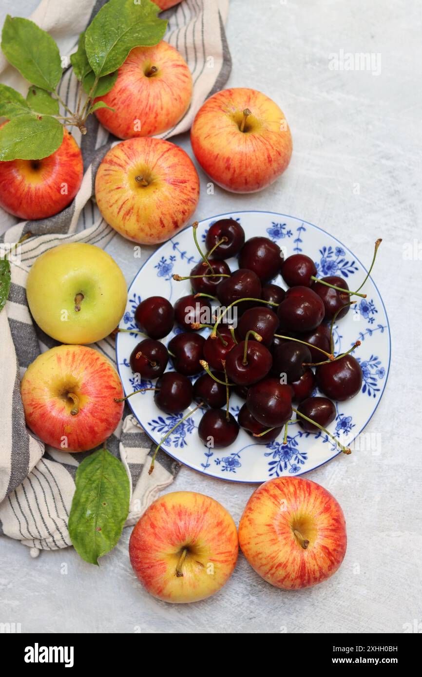 Rote Äpfel und Kirschen auf einem Teller auf hellem Hintergrund mit Kopierraum. Nahaufnahme der Sommerfrüchte. Fresh-Konzept. Reife rote Äpfel Stockfoto