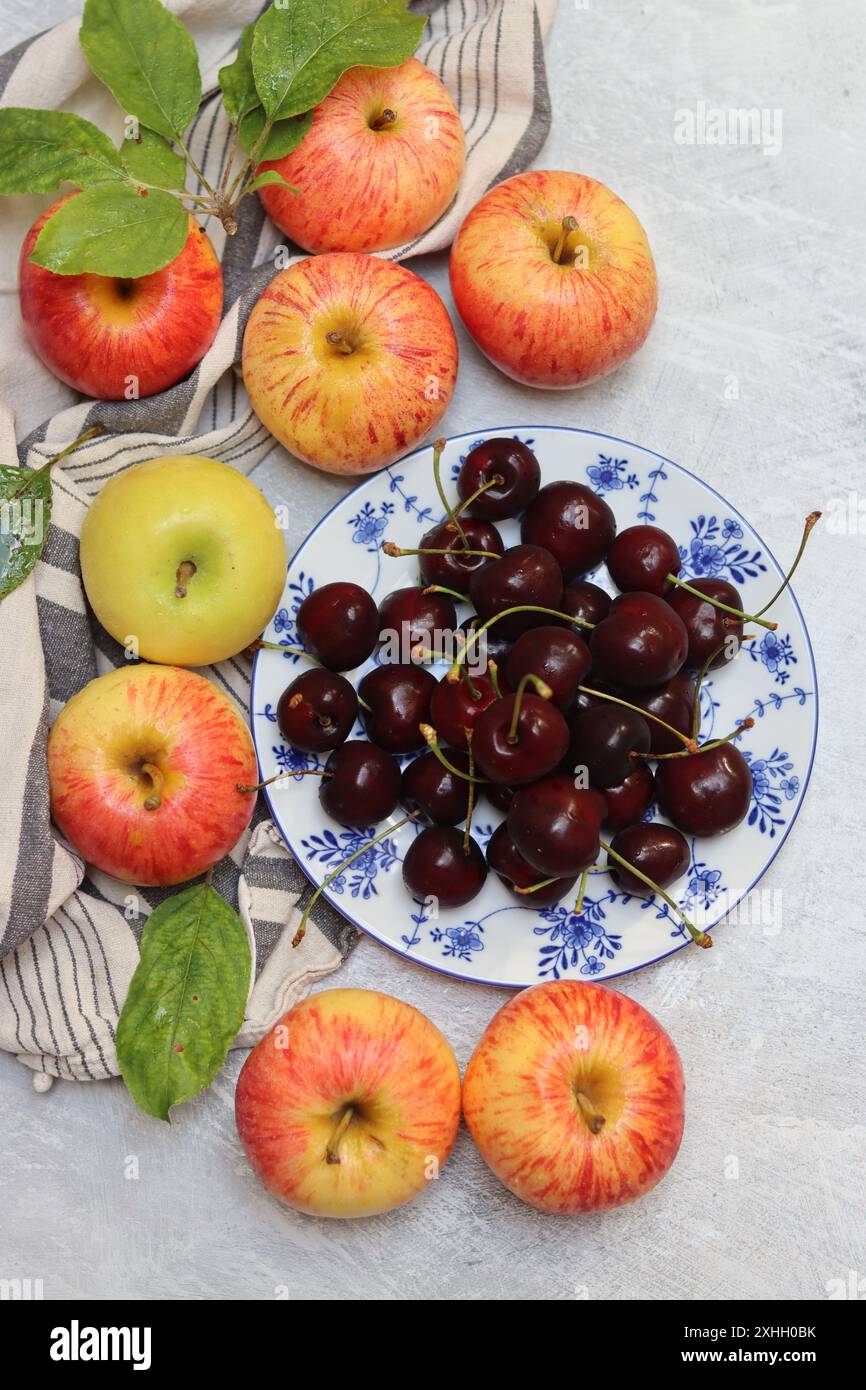 Rote Äpfel und Kirschen auf einem Teller auf hellem Hintergrund mit Kopierraum. Nahaufnahme der Sommerfrüchte. Fresh-Konzept. Reife rote Äpfel Stockfoto