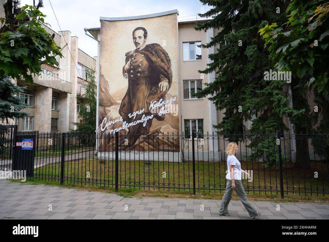 Die junge Frau geht vorbei an einem großen Porträt des berühmten russischen Dichters Lermontow, Pjatigorsk, der Region Stavropol, Russland. Resort City Street am Kaukasus im Sommer. Co Stockfoto