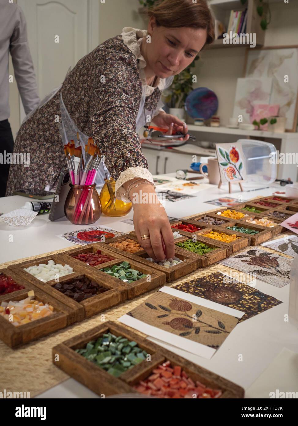 Vertikale Nahaufnahme einer Frau, die während eines Mosaikkunstkunstkunstkurses nach einem Vitrage-Glas greift. Stockfoto