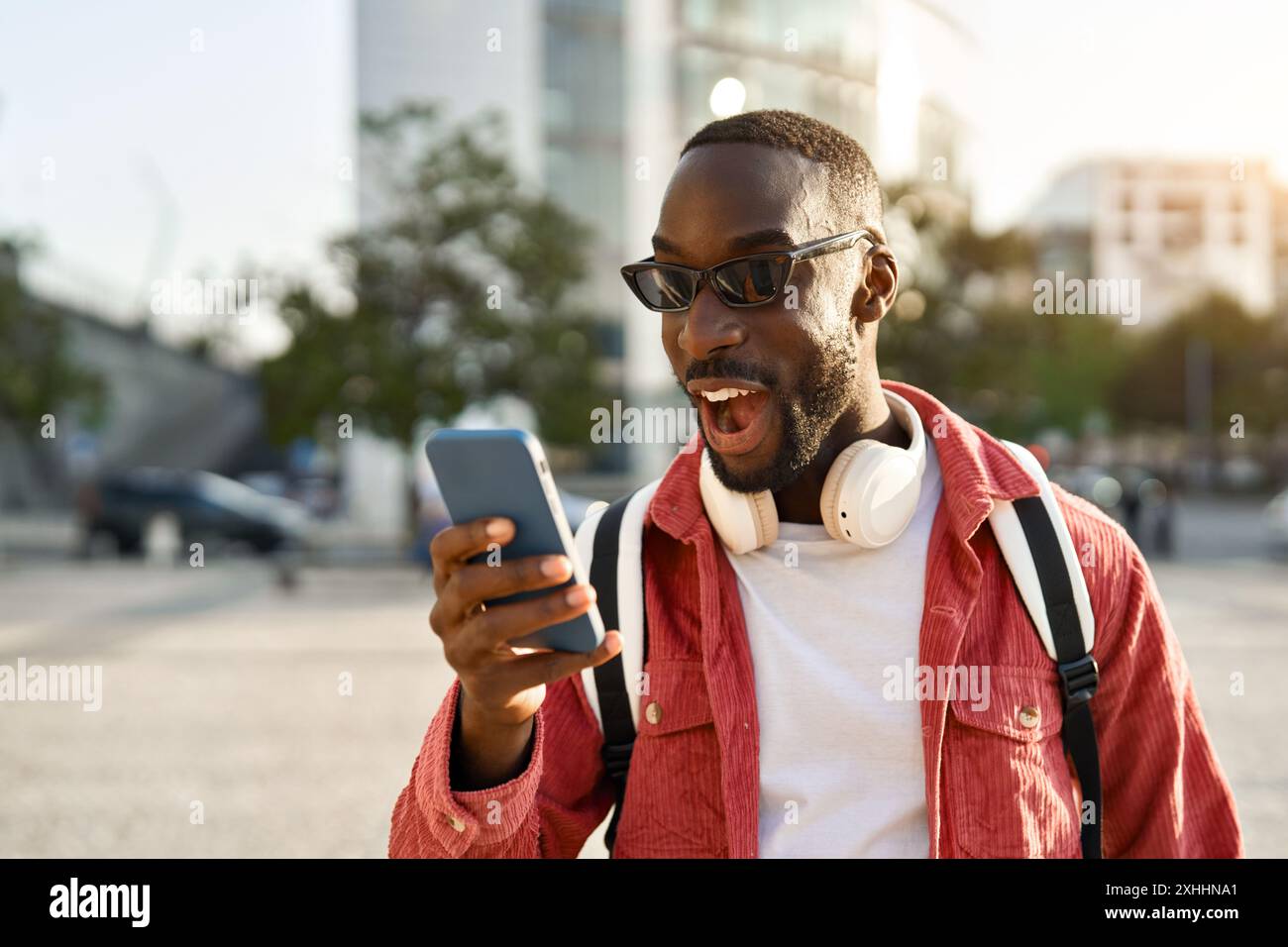 Staunender afrikanischer Mann, der auf der Stadtstraße steht und das Telefon überraschend ansieht. Stockfoto