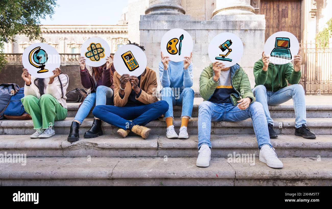 Verschiedene Gruppen von Schülern sitzen auf Stufen und halten kreisförmige Schilder mit Symbolen für verschiedene akademische Fächer. Das Konzept der Diversität im Bildungswesen Stockfoto