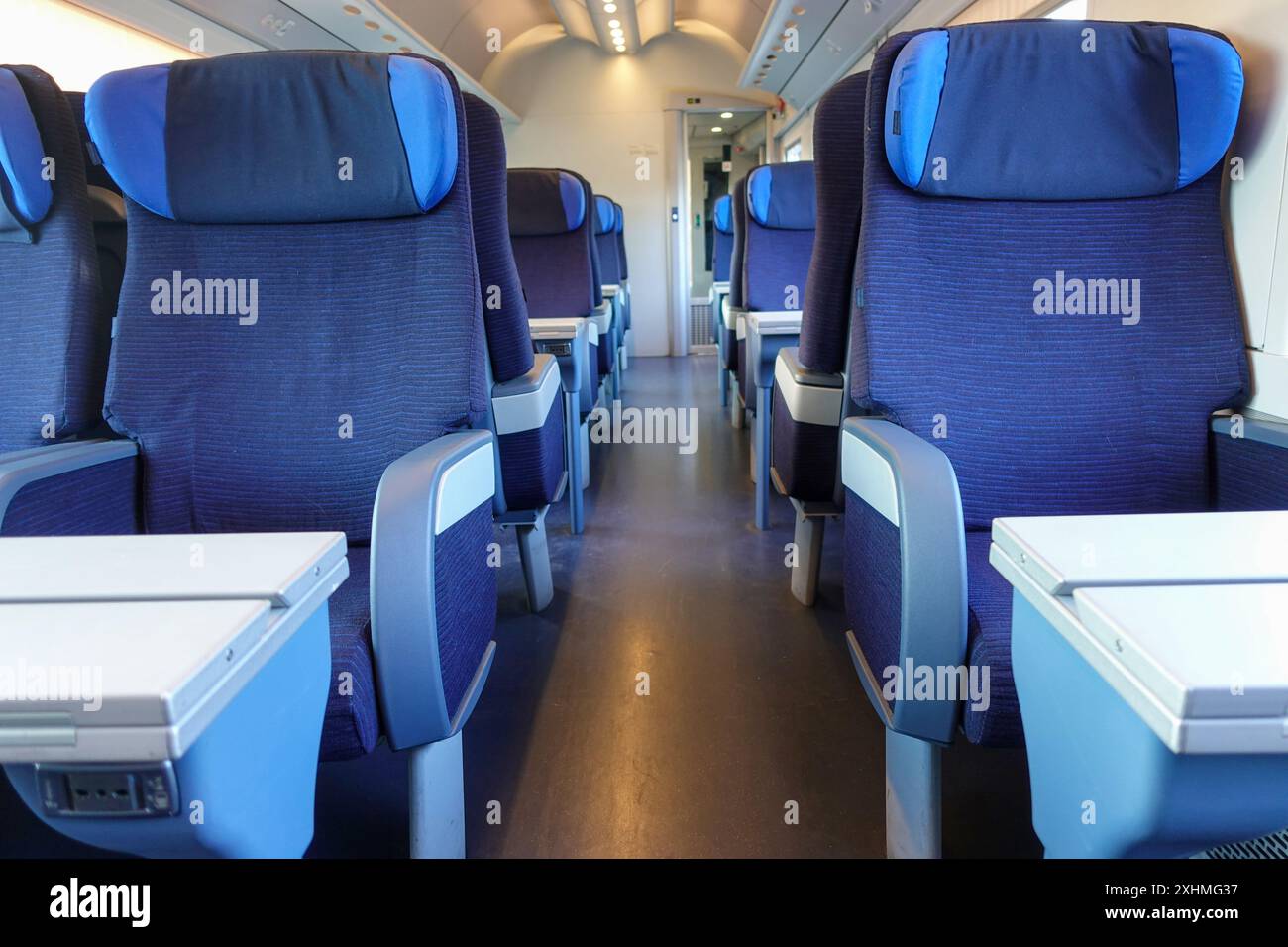 Reihen von leeren blauen Sitzen mit Kopfstützen und Klapptischen in einem modernen Hochgeschwindigkeitszug Stockfoto