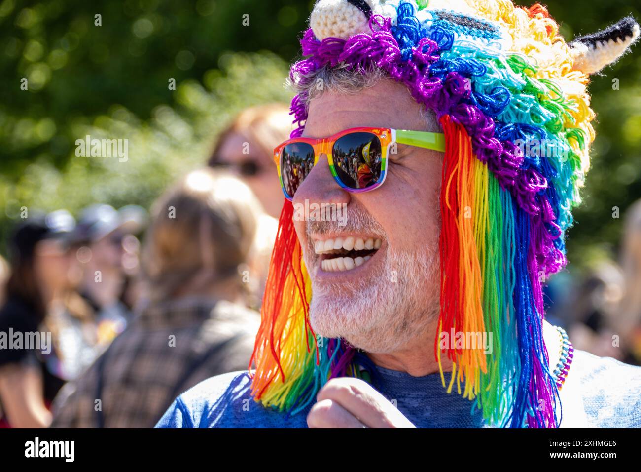 Ein Mann lächelt bei einer Stolz-Veranstaltung mit Regenbogensonnenbrille und Hut Stockfoto