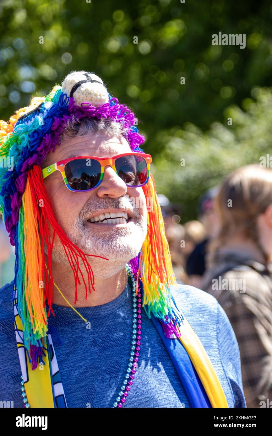Mann bei einer Stolz-Veranstaltung mit Regenbogensonnenbrille und buntem Hut Stockfoto