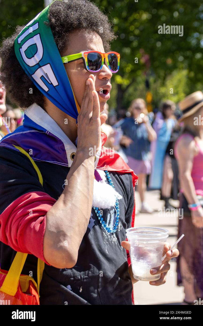 Ein Mann, der bei einer Pride-Veranstaltung anfeuert, trägt eine Regenbogensonnenbrille und einen Pride-Schal Stockfoto