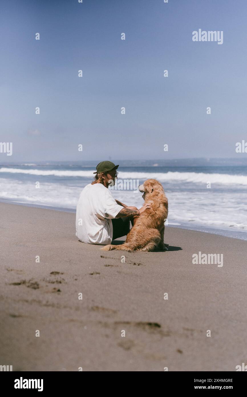 Der Mann sitzt am Meer am Strand mit goldenem Retriever-Hund. Stockfoto