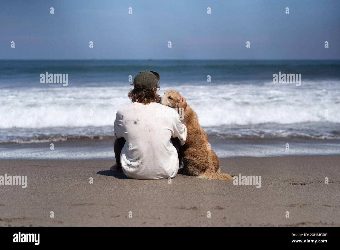 Der Mann sitzt am Meer am Strand mit goldenem Retriever-Hund. Stockfoto