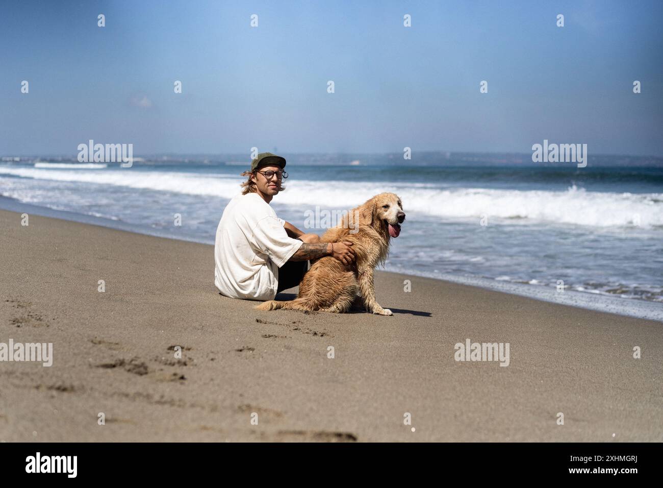 Der Mann sitzt am Meer am Strand mit einem goldenen Retriever-Hund. Stockfoto