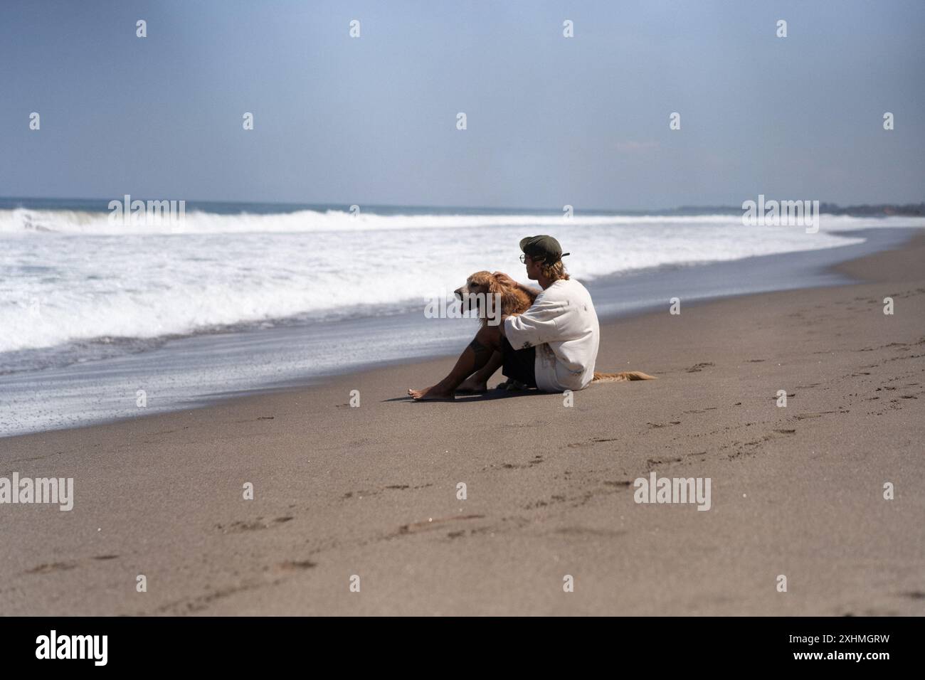 Der Mann sitzt am Meer am Strand mit goldenem Retriever-Hund. Stockfoto