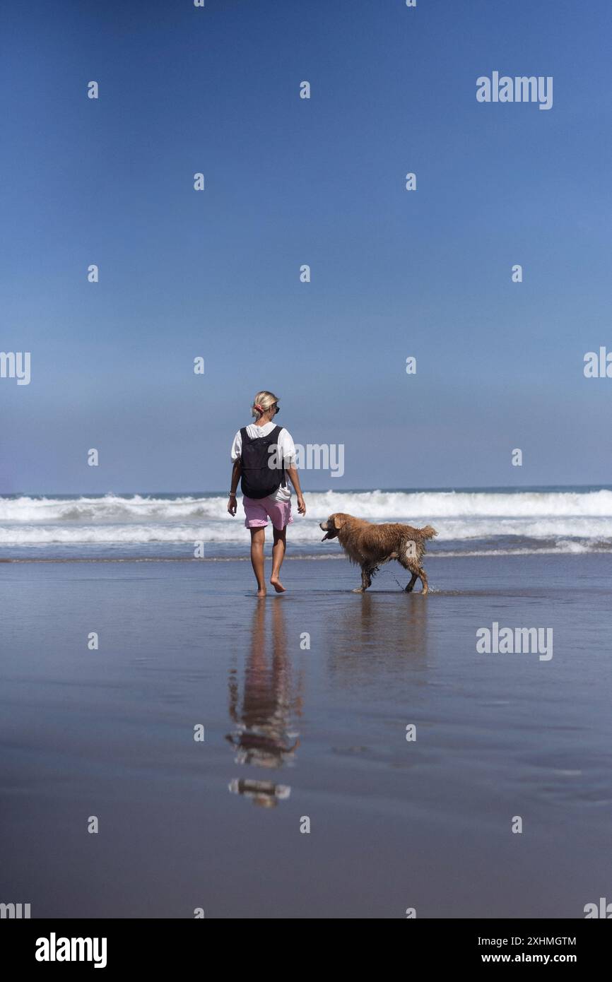 Eine Frau läuft mit ihrem goldenen Retriever-Hund am Strand entlang. Stockfoto