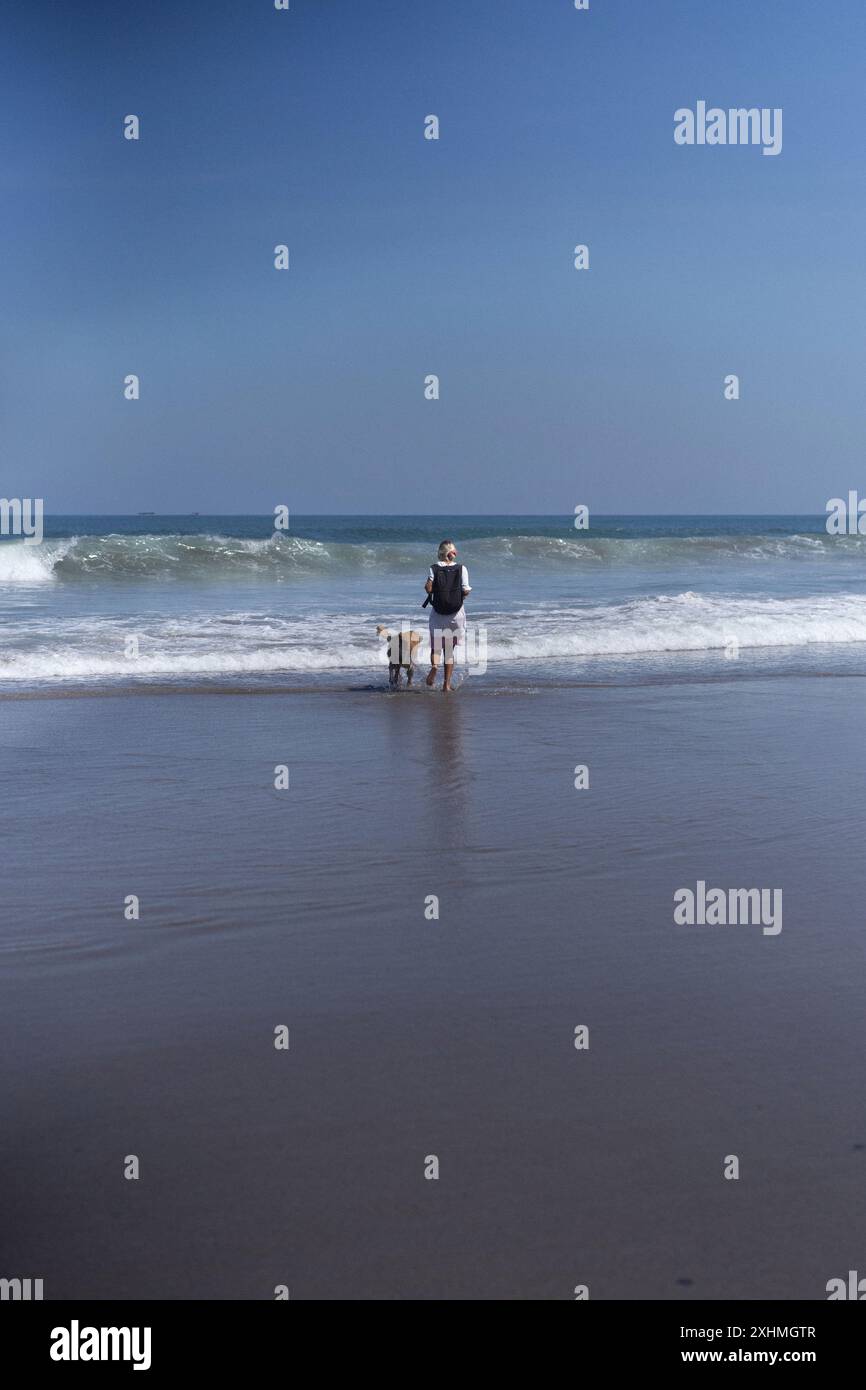 Eine Frau läuft mit ihrem goldenen Retriever-Hund am Strand entlang. Stockfoto