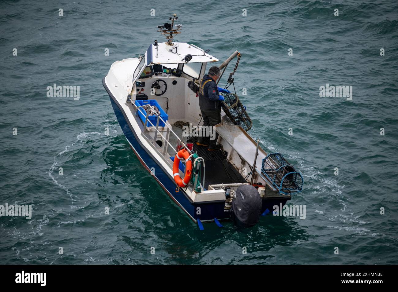 Kleines Fischerboot vor der Küste von Anglesey, Nordwales. Ein einziger Fischer inspiziert Hummertöpfe. Stockfoto