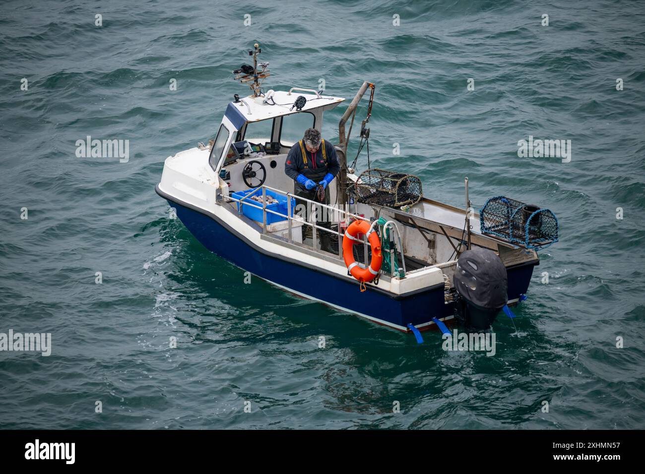 Kleines Fischerboot vor der Küste von Anglesey, Nordwales. Ein einziger Fischer inspiziert Hummertöpfe. Stockfoto