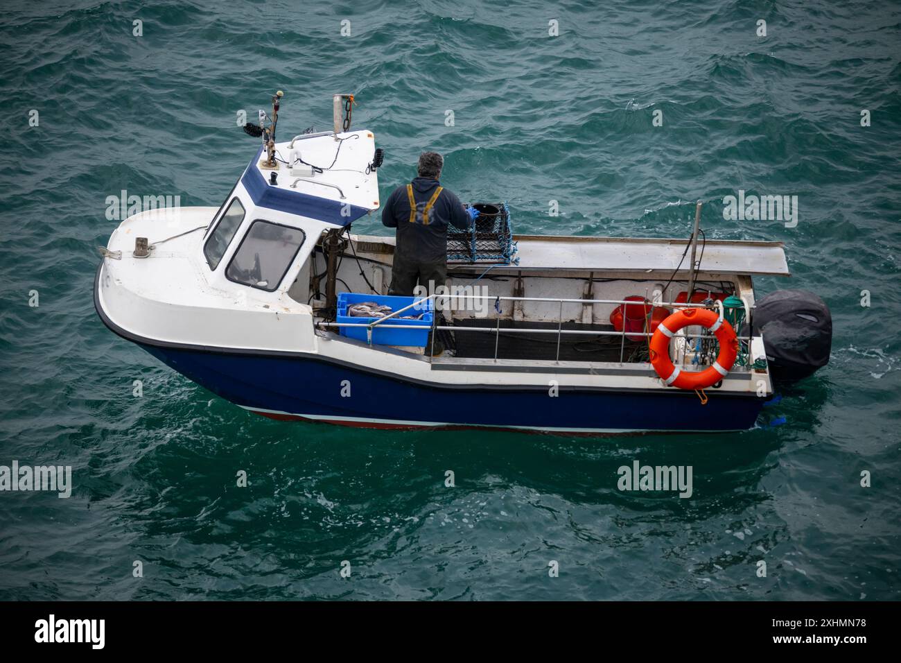 Kleines Fischerboot vor der Küste von Anglesey, Nordwales. Ein einziger Fischer inspiziert Hummertöpfe. Stockfoto