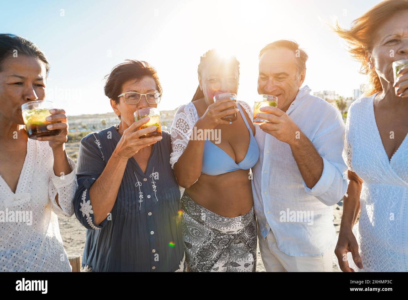 Ältere multirassische Freunde jubeln bei Sonnenuntergang am Strand mit Mojitos - Reife Leute, die Spaß während der Sommerferien haben - konzentrieren Sie sich auf afrikanische Frau fac Stockfoto
