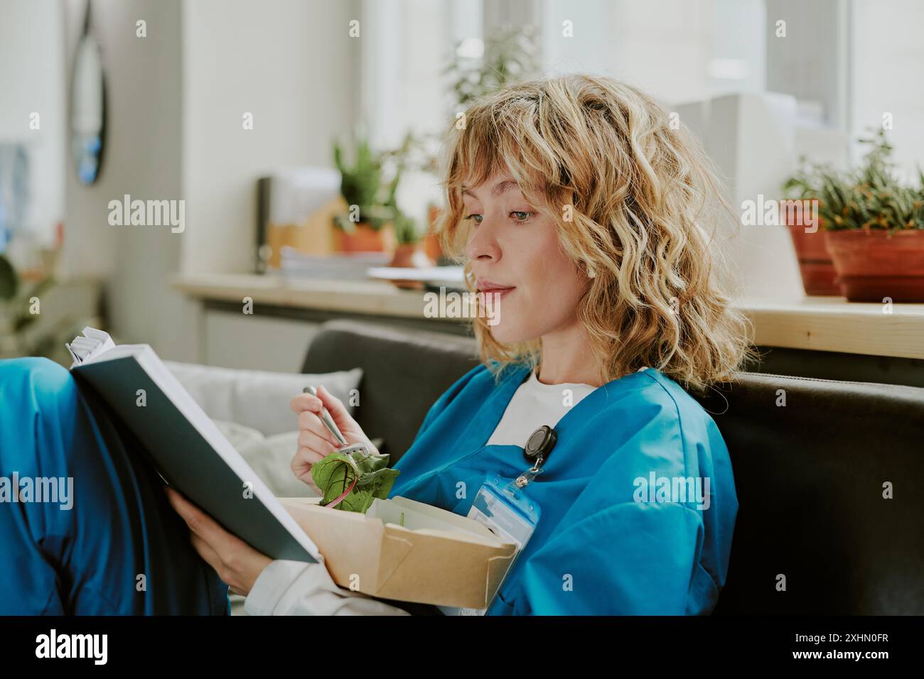 Profilaufnahme einer jungen kaukasischen Krankenschwester, die während ihrer Pause im Bereitschaftsraum Salat isst Stockfoto
