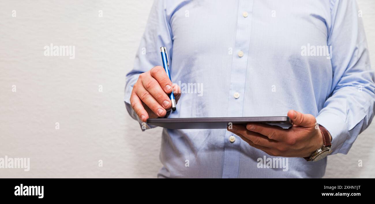 Ein nicht erkennbarer Mann berührt ein Tablet mit einem Stift. Er trägt ein blaues Hemd und weiße Knöpfe. Stockfoto