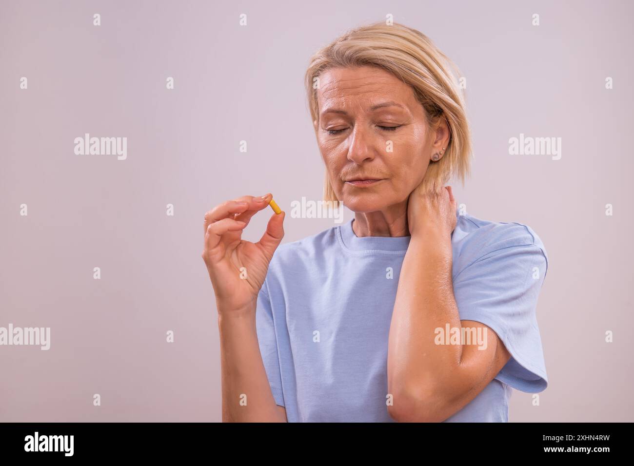 Reife Frau nimmt Pillen gegen Nackenschmerzen ein. Stockfoto