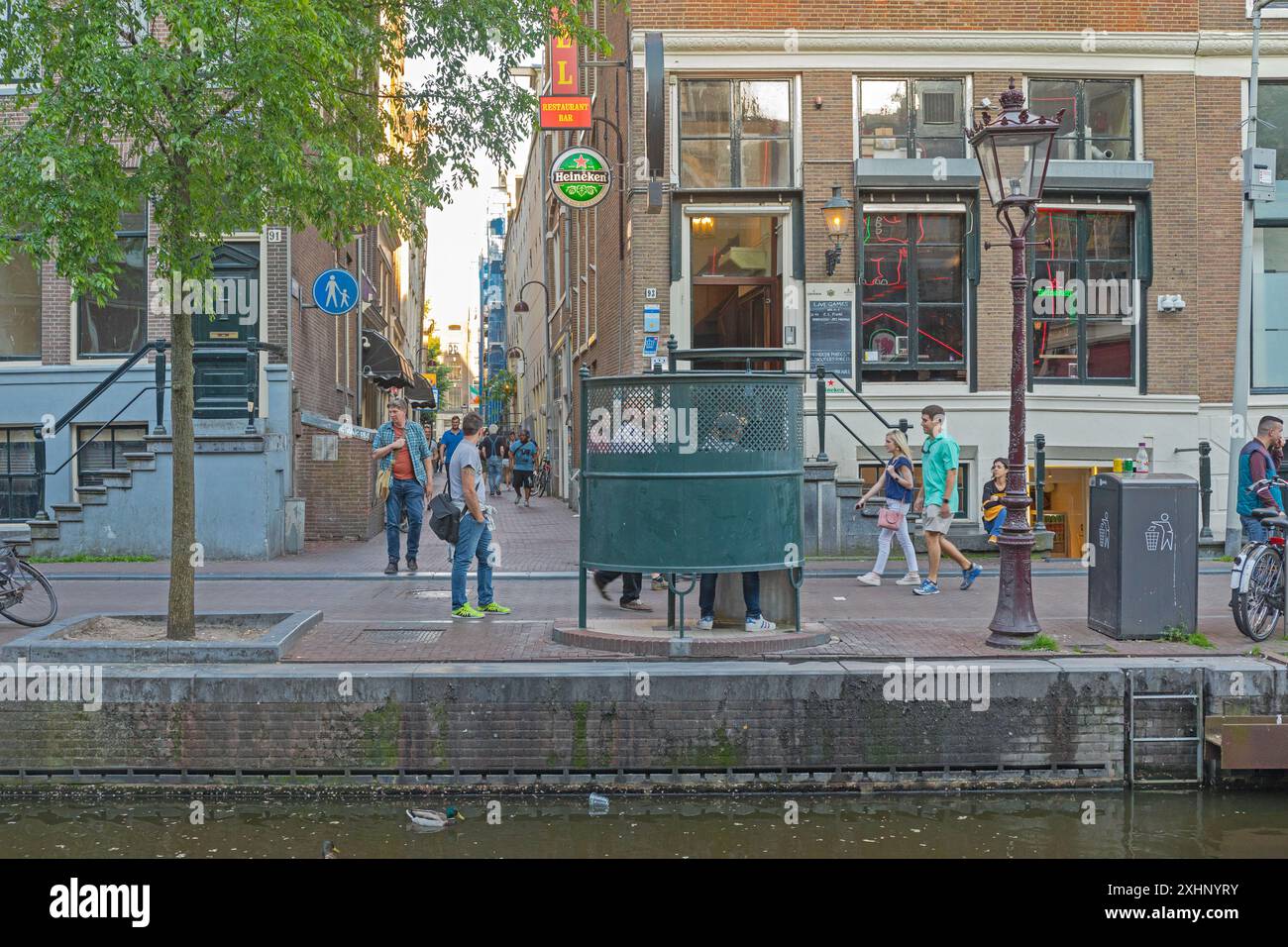 Amsterdam, Niederlande - 15. Mai 2018: Menschen, die in der Oudezijds Achterburgwal Street laufen, öffentliche Toilette Curl Heineken Bar Frühlingstag im Rotlichtdistri Stockfoto