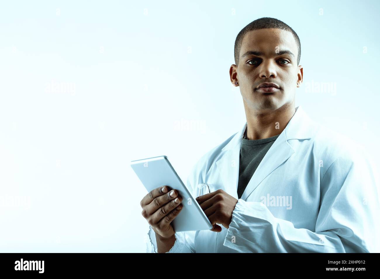 Junger Datenwissenschaftler, der sich auf Deep Learning und LLM-Analyse spezialisiert hat und ein digitales Tablet hält. In einem weißen Labormantel gekleidet, sein ernster Ausdruck Ref Stockfoto