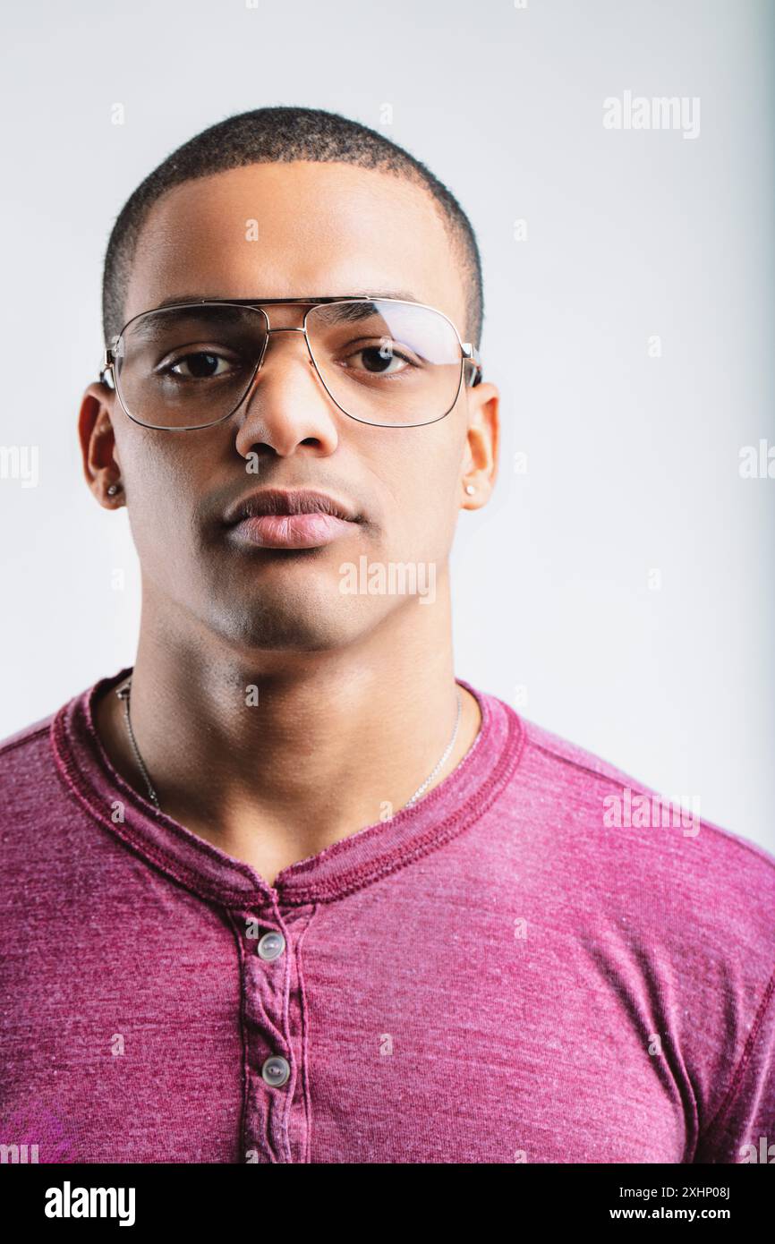 Junger Mann mit ernstem Ausdruck, mit Fliegerbrille und einem kastanienbraunen henley-Hemd. Sein fokussierter Look und seine lässige Kleidung deuten auf Selbstvertrauen und eine Re hin Stockfoto
