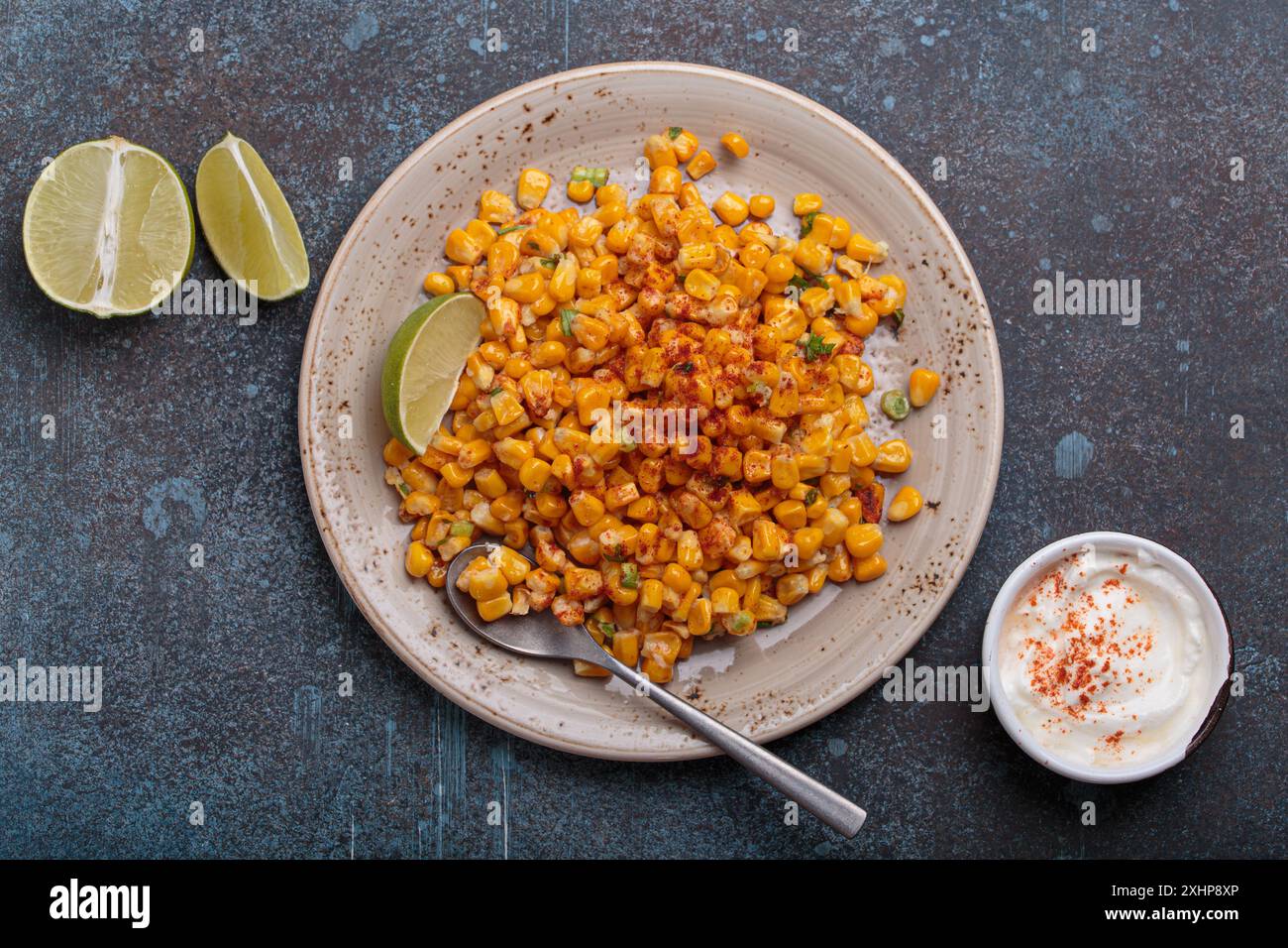 Teller mit Esquites mexikanischem Streetmaissalat mit Chili, Mayonnaise und Limette auf dunklem Steinhintergrund Stockfoto