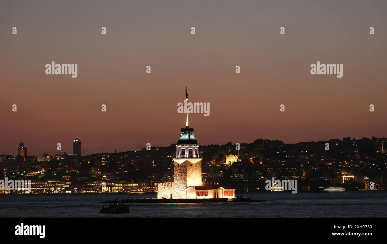 Langzeitaufnahme des Mädchenturms - Kız Kulesi in Istanbul. Die unscharfe Bewegung eines Bootes auf dem Wasser verleiht der Nacht ein dynamisches Element. Stockfoto