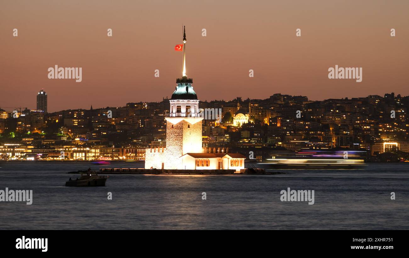 Langzeitaufnahme des Mädchenturms - Kız Kulesi in Istanbul. Die unscharfe Bewegung eines Bootes auf dem Wasser verleiht der Nacht ein dynamisches Element. Stockfoto