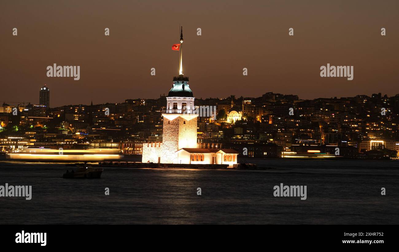 Langzeitaufnahme des Mädchenturms - Kız Kulesi in Istanbul. Die unscharfe Bewegung eines Bootes auf dem Wasser verleiht der Nacht ein dynamisches Element. Stockfoto