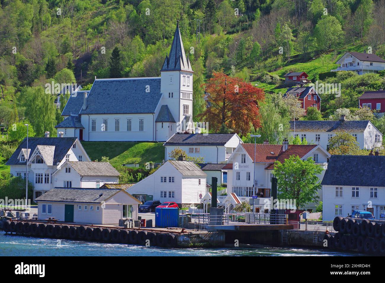 Dorf mit Kirche auf einem grünen Hügel, umgeben von Holzhäusern und einem Fähranleger, Utne, Hardanger, Hardangerfjord, Norwegen Stockfoto