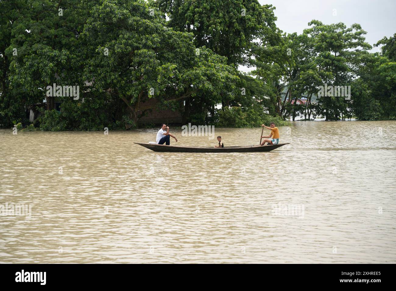 Morigaon, Indien. 4. Juli 2024. Die Menschen fahren mit einem Boot, um ein überflutetes Gebiet in einem von Überschwemmungen betroffenen Dorf im Bezirk Morigaon in Indien zu überqueren Stockfoto Morigaon, Indien. 4. Juli 2024. Die Menschen fahren mit einem Boot, um ein überflutetes Gebiet in einem von Überschwemmungen betroffenen Dorf im Bezirk Morigaon in Indien zu überqueren Stockfoto