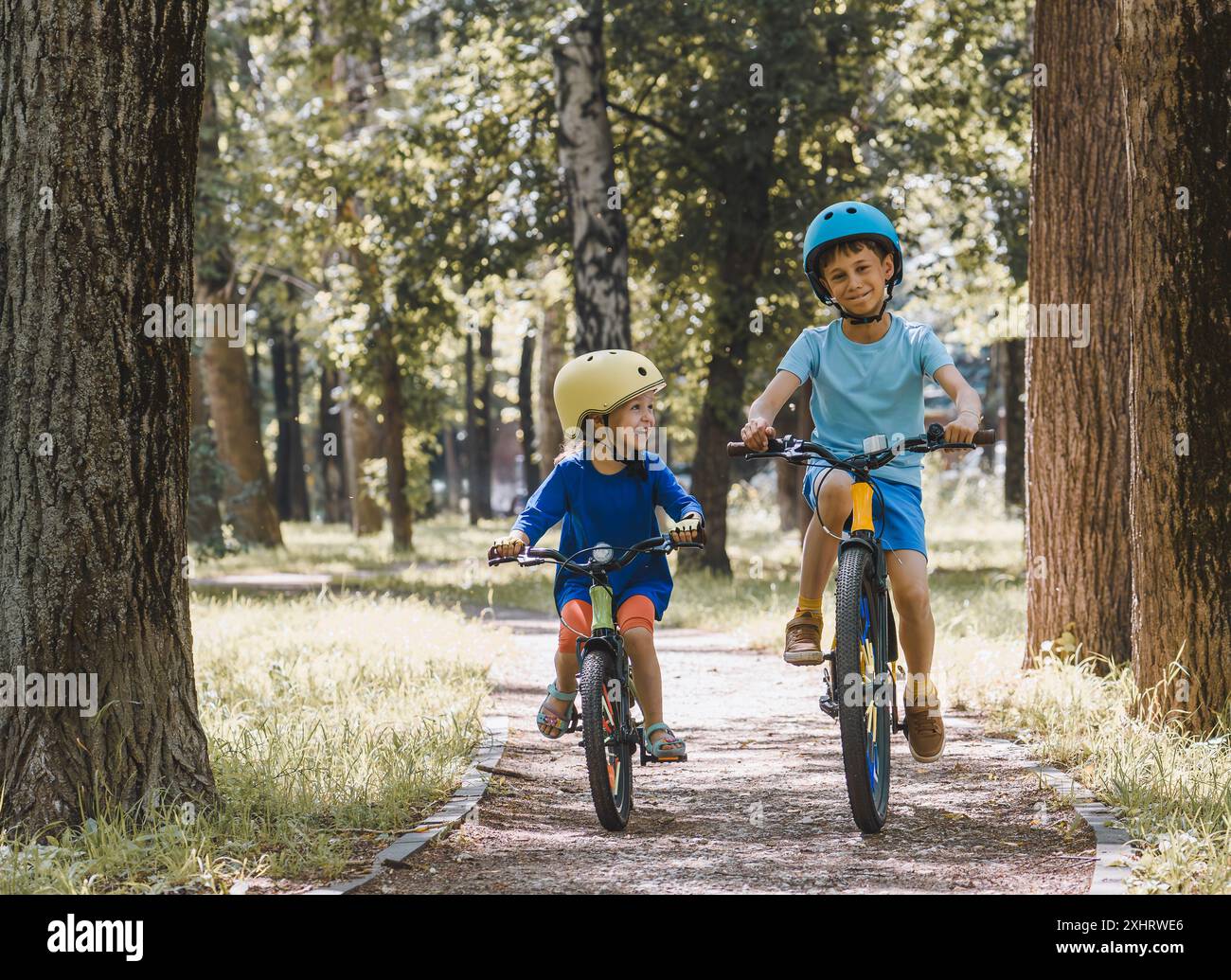 Glückliche Kinder, die am heißen Sommertag im Stadtpark Fahrrad fahren Stockfoto