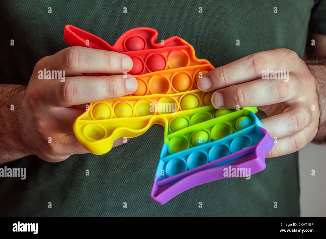 Hände halten Regenbogenblase mit sensorischem Anti-Stress-Squeeze-Spielzeug in Einhornform Stockfoto