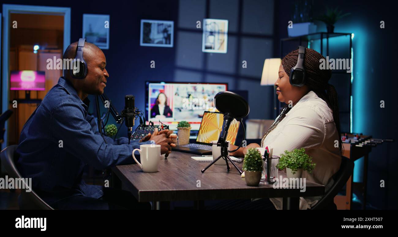 Content Creator hat während des Podcasts gute Gespräche mit Gästen. Gastgeber genießt Kaffee zusammen mit einer fröhlichen Frau live im Apartmentstudio während der Internetshow, Zoom out shot Stockfoto