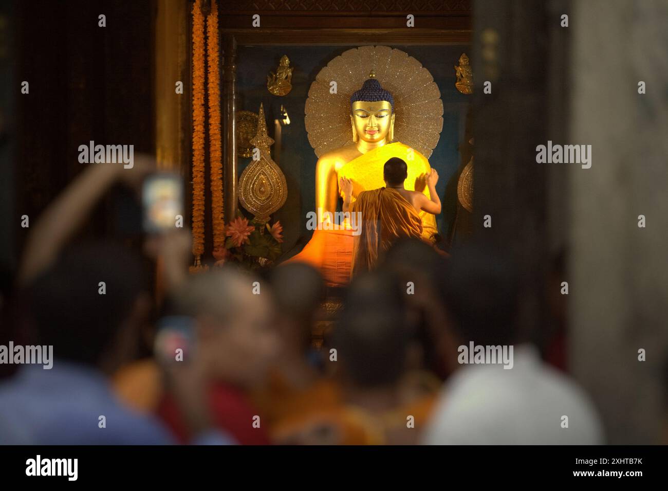 Ein diensthabender Mönch, der die Statue des heiligen Goldenen Buddha mit einem neuen Gewand im Inneren des Kammerschreins des Mahabodhi-Tempels in Bodh Gaya, Bihar, Indien bedeckt. Stockfoto